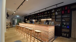 Eine moderne Bar mit einer Holztresen, Hockern und Regalen voller Flaschen und Gläsern.