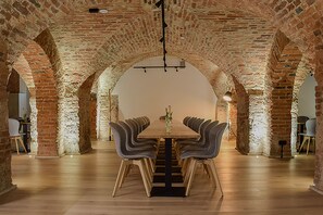 Une longue table à manger, entourée de chaises, dans une pièce ornée d’arches en briques et dotée d’un plancher en bois.