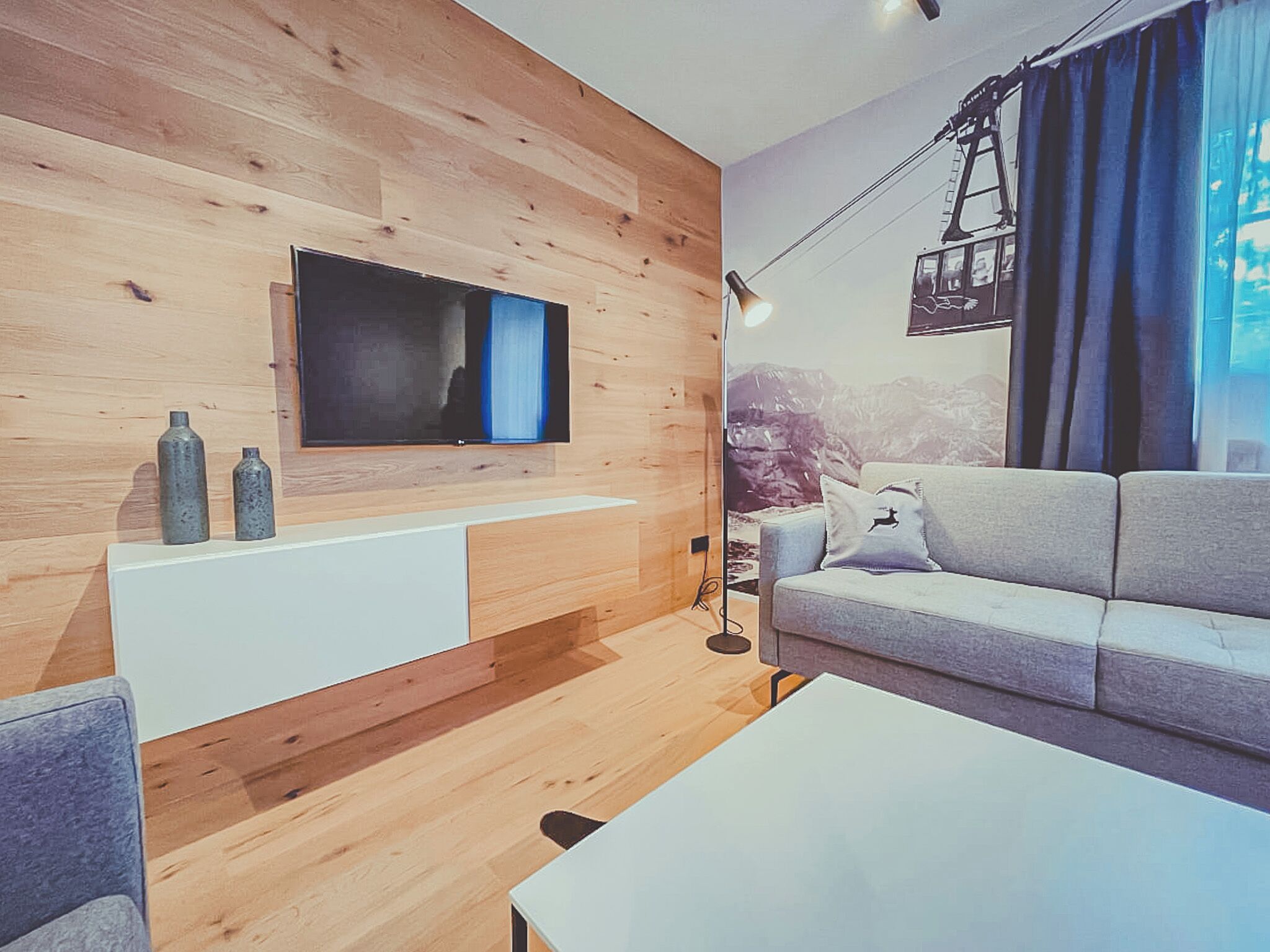 Una sala de estar moderna con una pared de madera, un televisor de pantalla plana, un sofá, una mesa de centro y una lámpara.