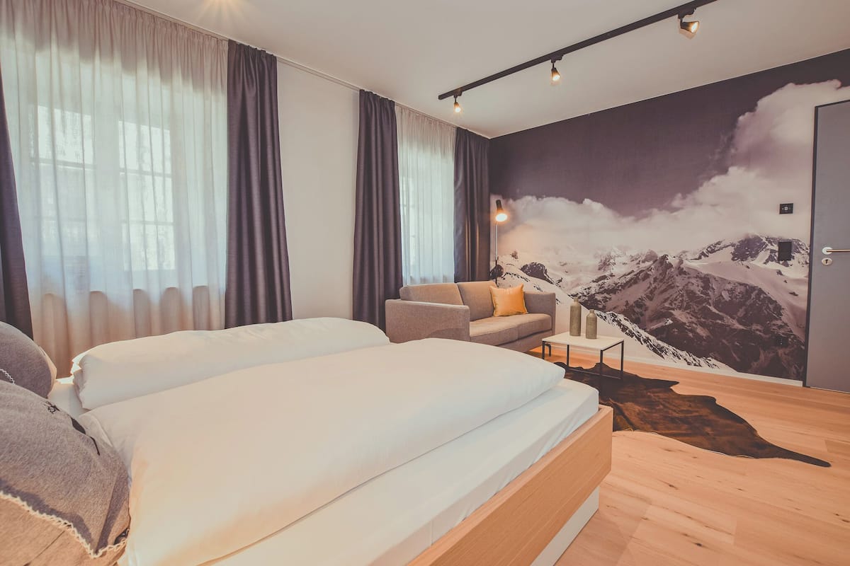 Un dormitorio moderno con una cama grande, un sofá y un mural de montañas en la pared.