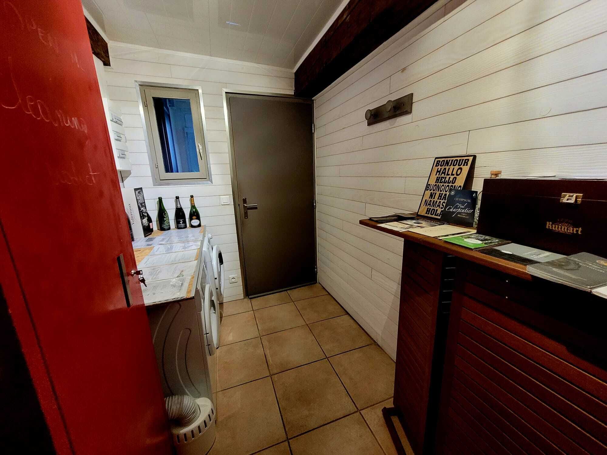 Un couloir étroit avec une porte, une petite fenêtre et un comptoir d’accueil avec une enseigne.