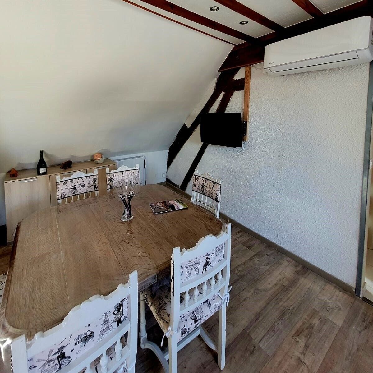 A dining area with a wooden table and white chairs, a whiteboard on the wall, and an air conditioning unit.