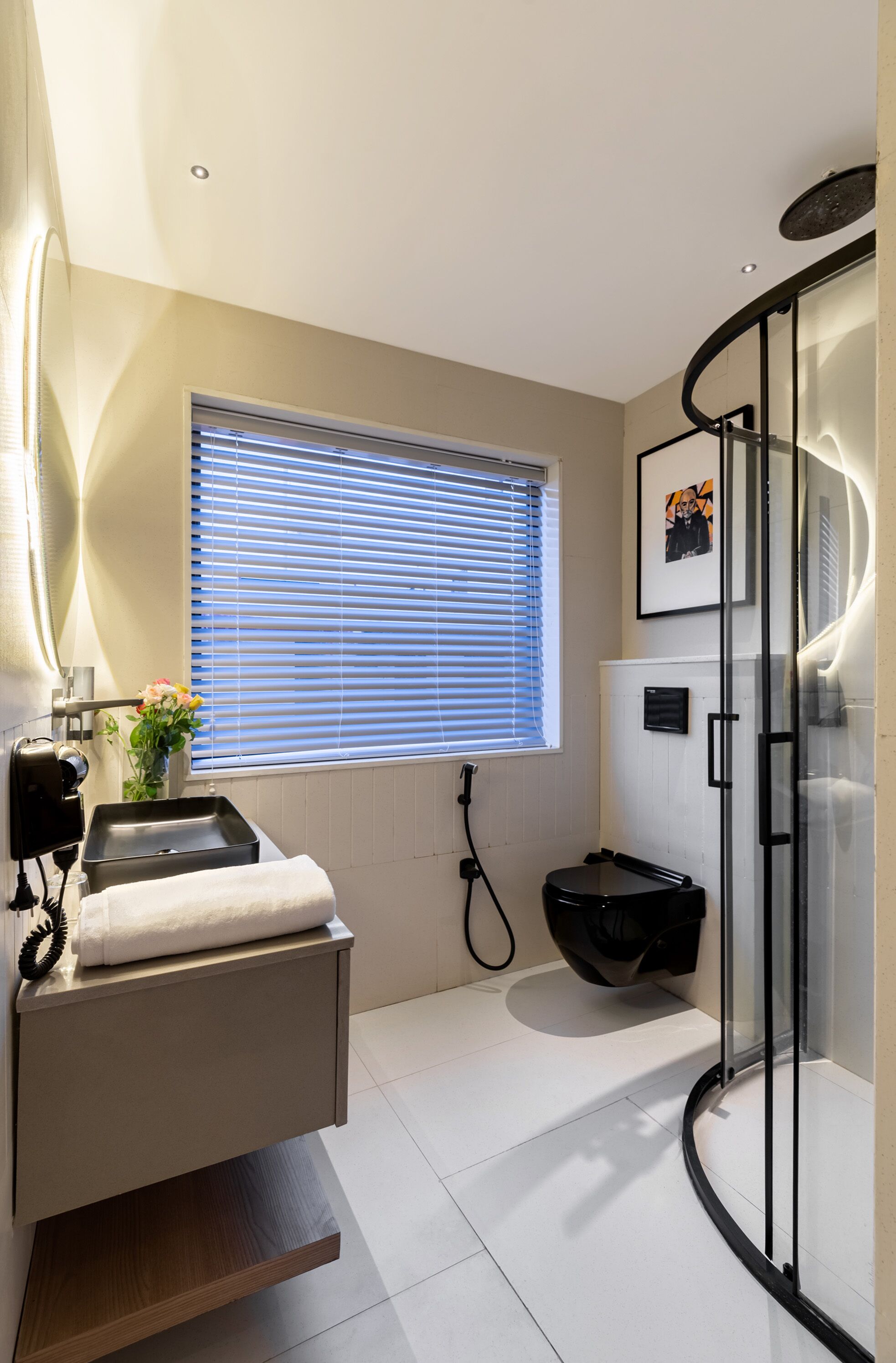 A modern bathroom with a glass shower enclosure, a built-in sink with a towel, and a window with blinds.