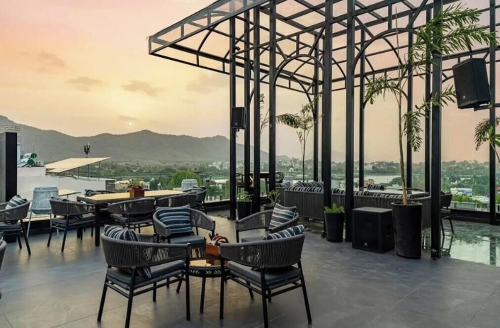 Terraza exterior con mobiliario de mimbre y cerramiento de vidrio, con vistas a montañas lejanas y el paisaje urbano.