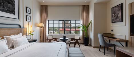 A hotel room with a large bed, a desk, a chair, a small table, and a potted plant.