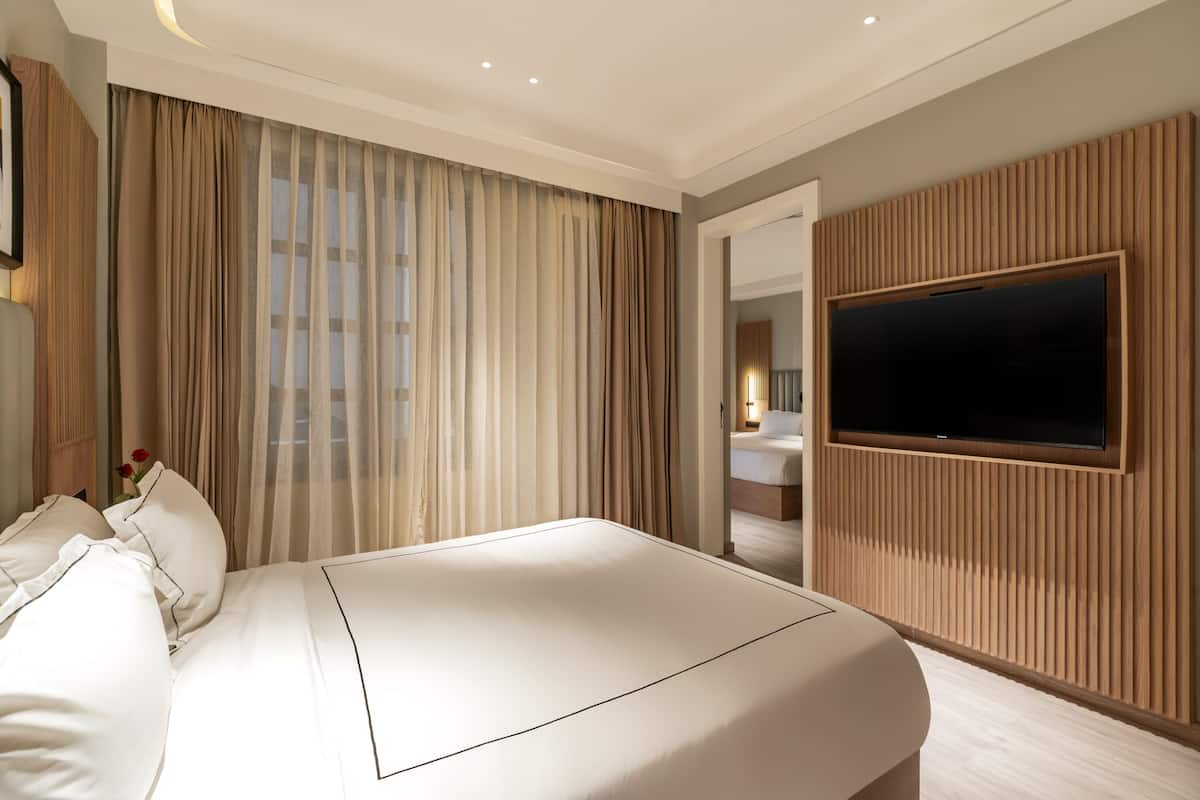 Una habitación de hotel moderna con una cama grande, un televisor de pantalla plana montado en la pared y vistas al baño a través de una puerta abierta.