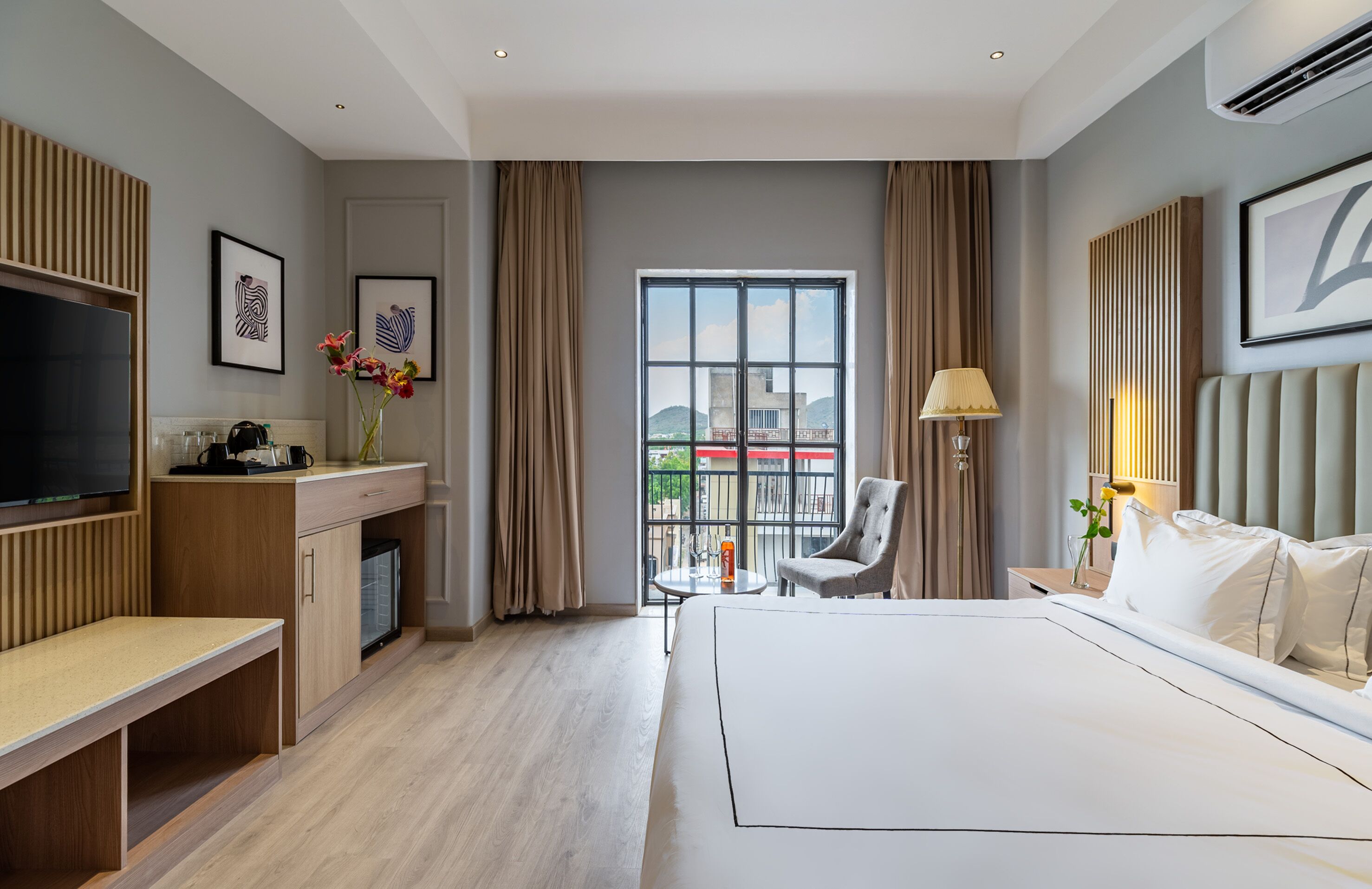 Una habitación de hotel moderna con una cama grande, un escritorio con televisor, una silla y un balcón con vistas.