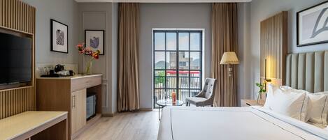 Una habitación de hotel moderna con una cama grande, un escritorio con televisor, una silla y un balcón con vistas.