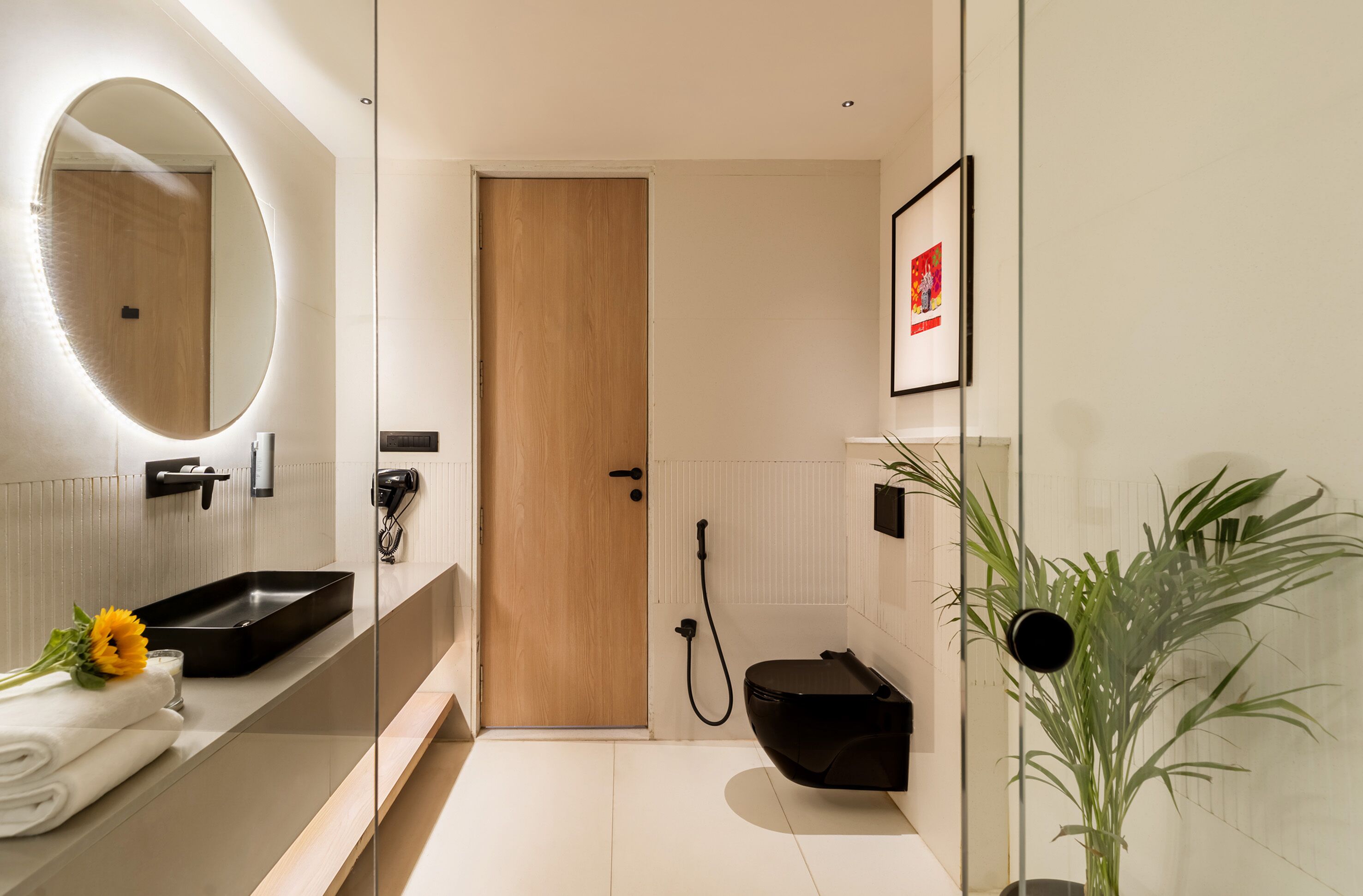 Ein modernes Badezimmer mit Holztür, Waschbecken in Schwarz, Spiegel, Dusche und einer Zimmerpflanze.