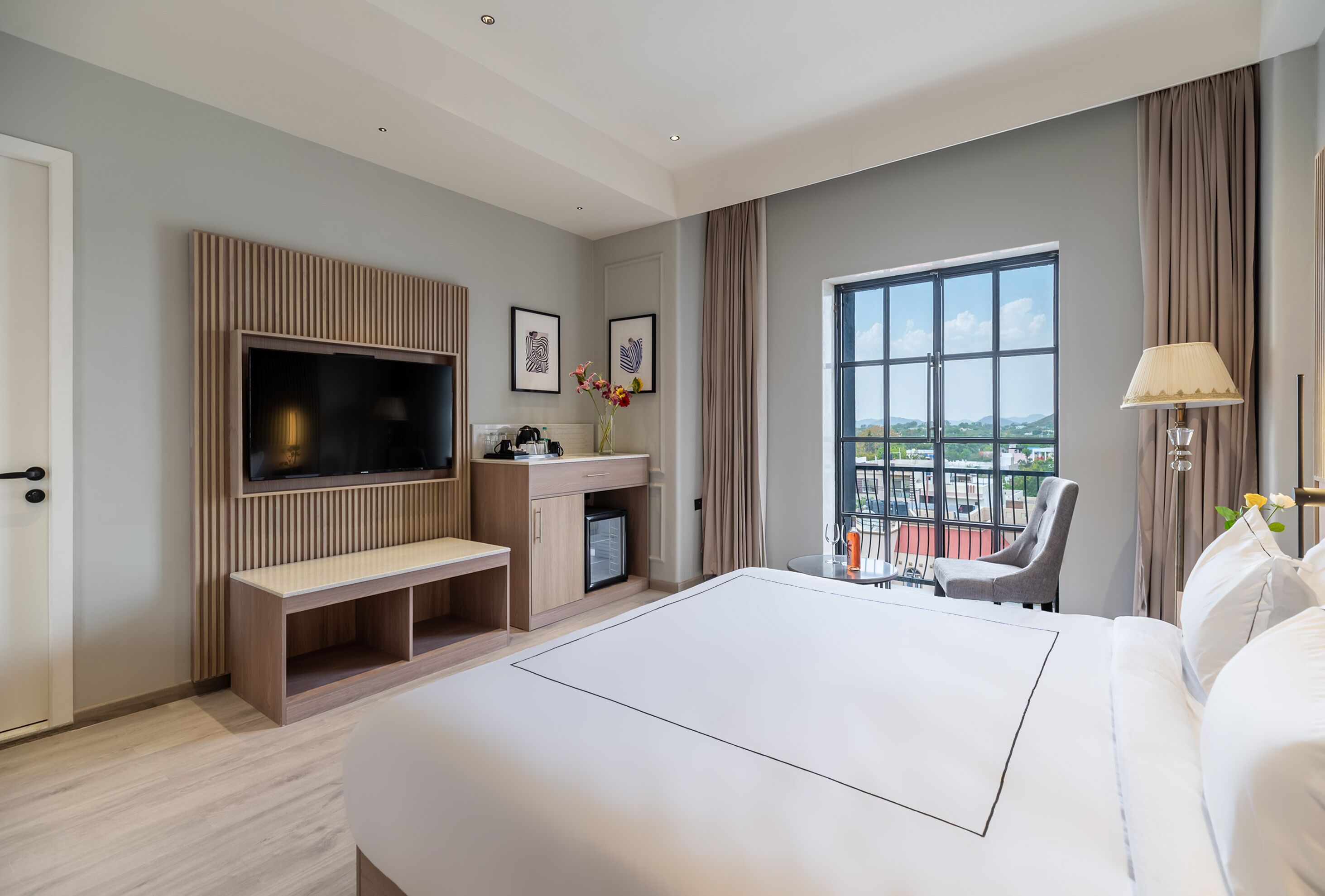 A modern hotel room with a large bed, a TV, a small desk, and a balcony with a view.