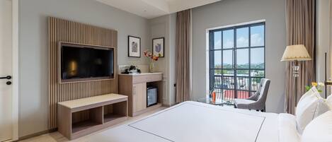 A modern hotel room with a large bed, a TV, a small desk, and a balcony with a view.