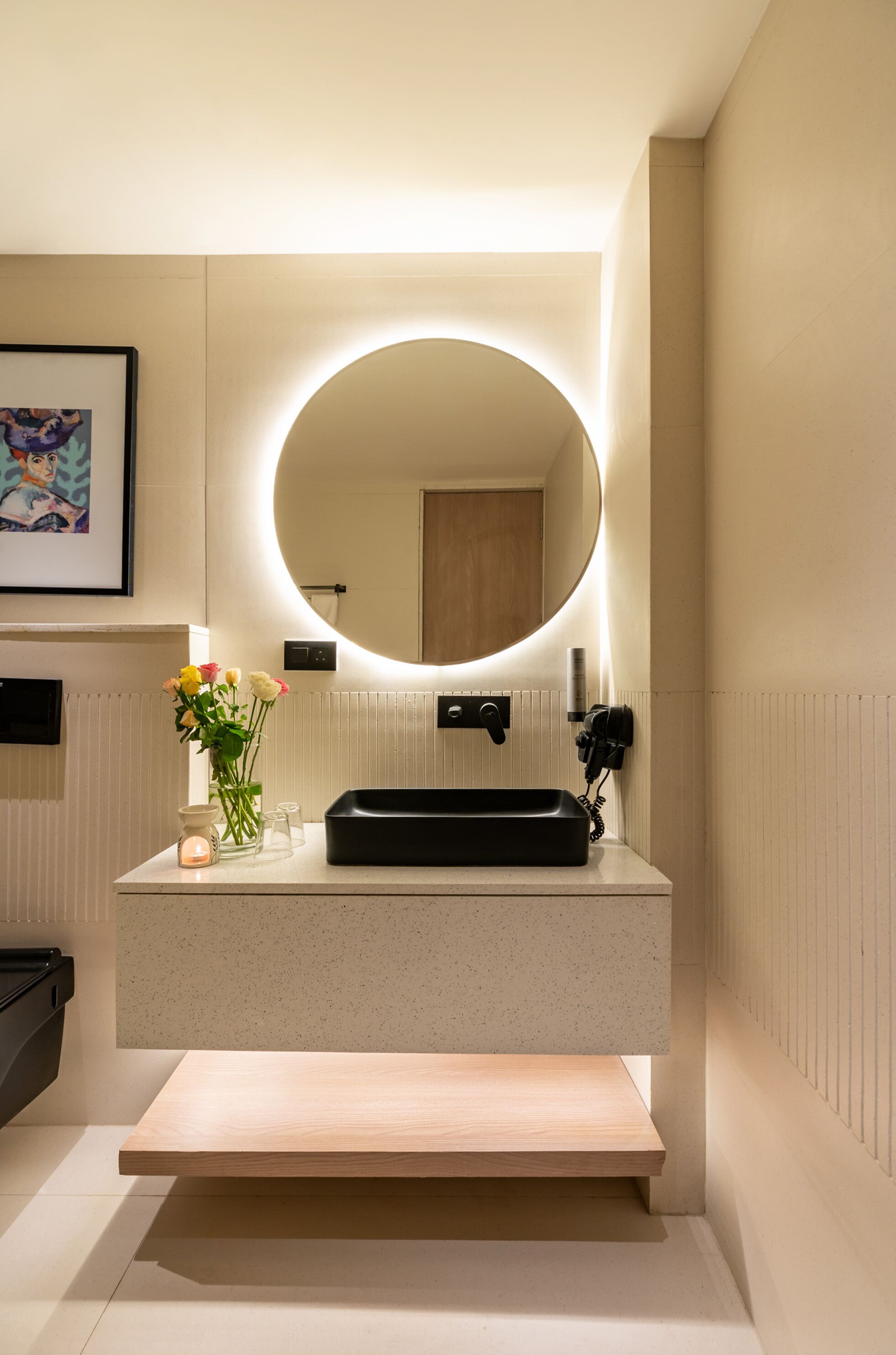 A modern bathroom with a round mirror, a black sink, and a vase of flowers on the countertop.