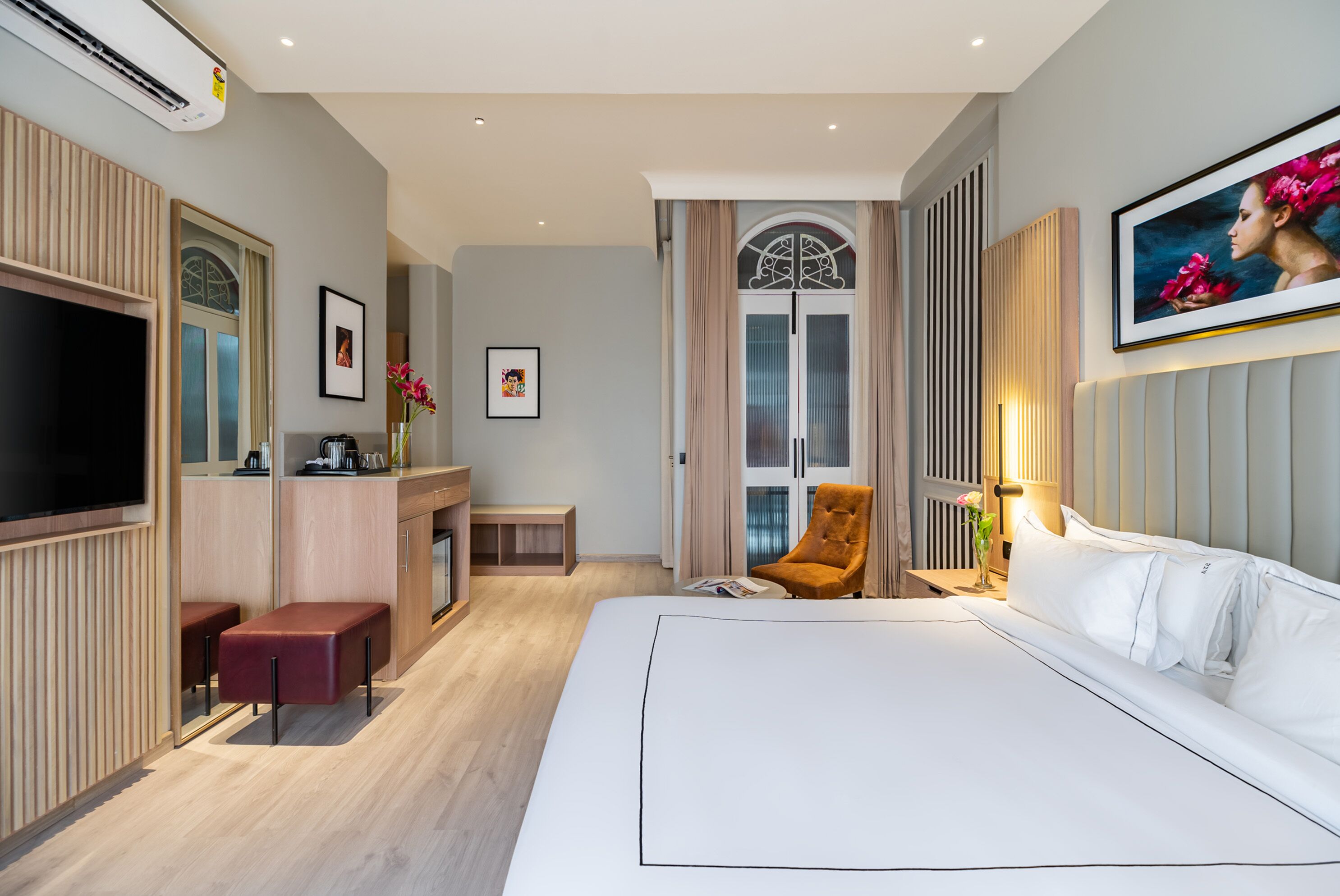 Een hotelkamer met een groot bed, een televisie, een bureau met stoel, een kleine tafel en een raam met gordijnen.