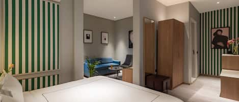 Een moderne hotelkamer met een groot bed, een zithoek met een bank en fauteuils, een klein tafeltje en een houten garderobe.