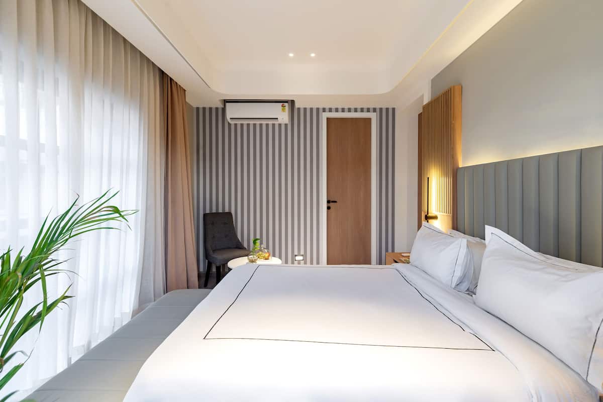 Una habitación de hotel moderna con una cama grande, una silla, una mesita con una planta y una puerta.