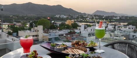 Une table dressée avec divers plats et boissons, offrant une vue sur un paysage urbain avec des montagnes en arrière-plan.