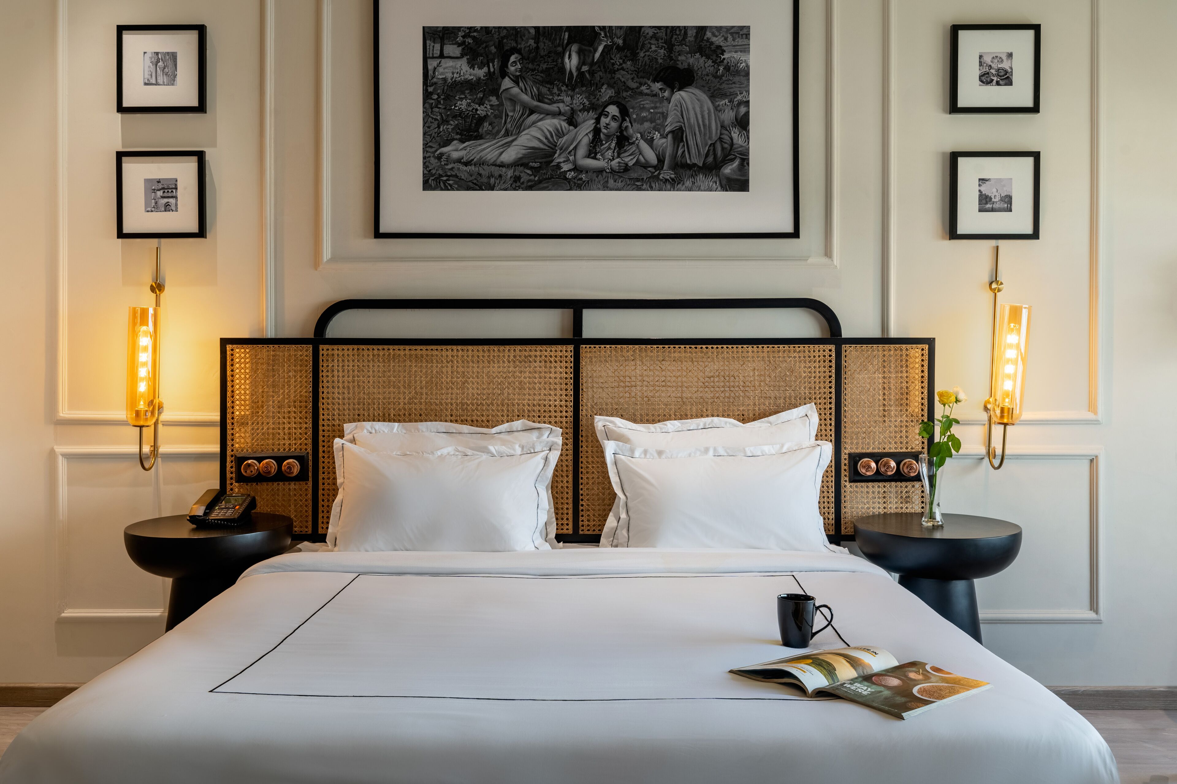 A hotel room with a large bed, two bedside tables with lamps, framed pictures on the wall, and a large painting above the bed.