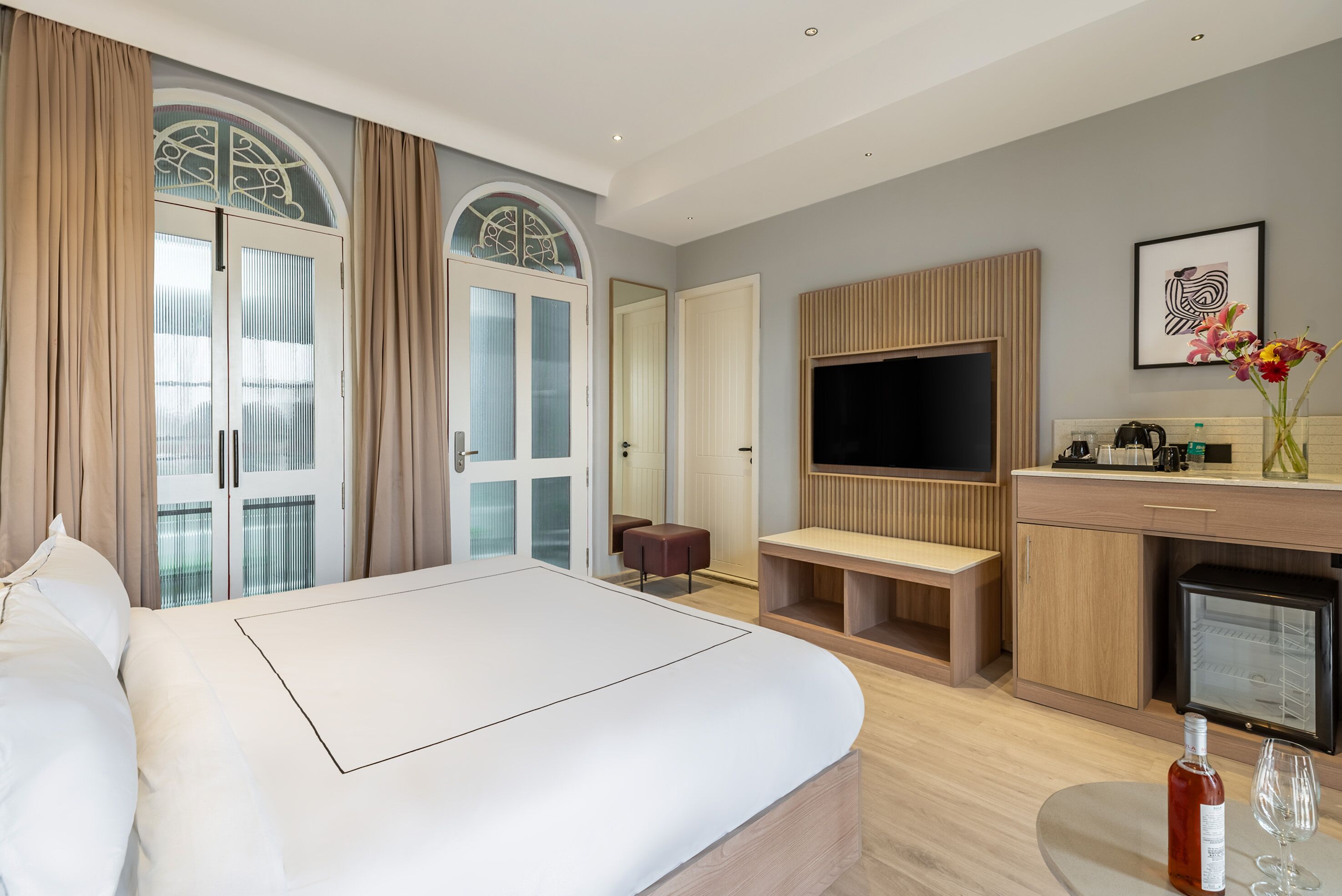 Ein modernes Hotelzimmer mit einem großen Bett, einem Fernseher, einer kleinen Küchenzeile und einer Sitzecke.
