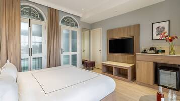 Ein modernes Hotelzimmer mit einem großen Bett, einem Fernseher, einer kleinen Küchenzeile und einer Sitzecke.