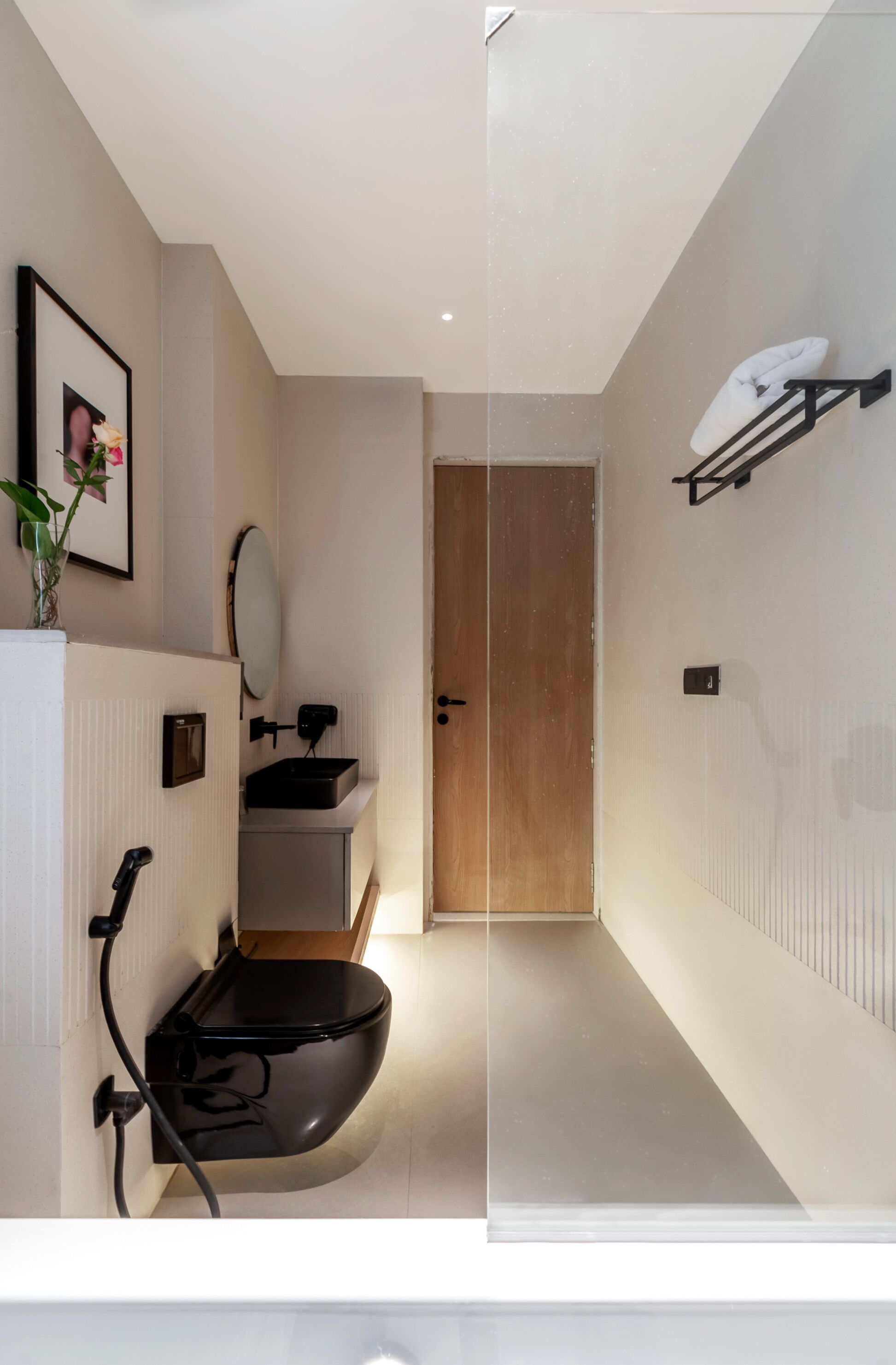 A modern bathroom with a toilet, sink, and mirror. There is a wooden door leading to another room.