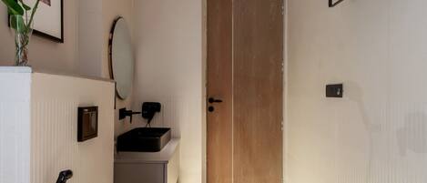 A modern bathroom with a toilet, sink, and mirror. There is a wooden door leading to another room.