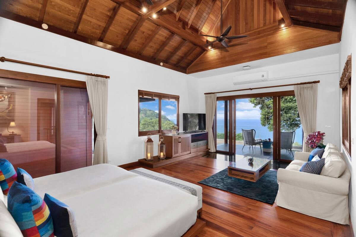 Una habitación amplia con una cama grande, un sofá, un televisor y un balcón con vista al mar.