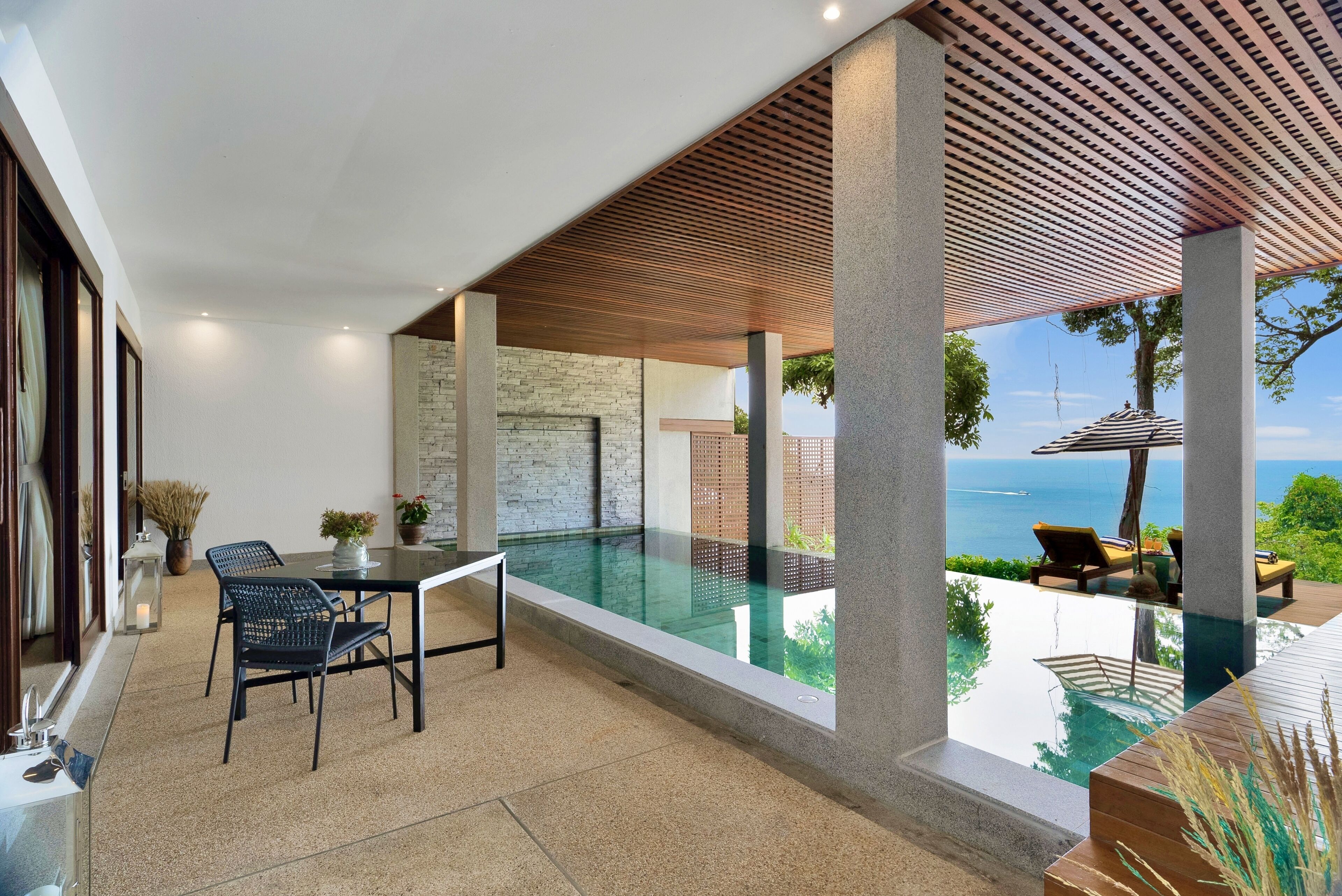 A modern outdoor pool area with a clear view of the sea, a table with chairs, and a pergola structure.