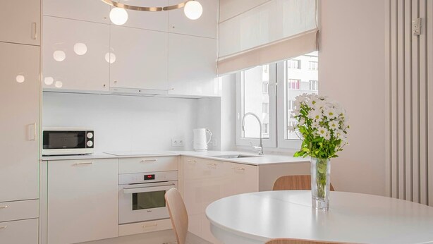 Et moderne køkken med hvide skabe, indbygget mikroovn, ovn og et rundt spisebord med stole.