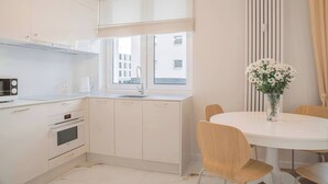 Et moderne køkken med hvide skabe, en indbygget ovn og et spiseområde med et rundt bord og stole.