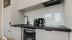 Una cocina moderna con gabinetes blancos, encimera negra, lavavajillas y cafetera.