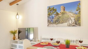 A dining area with a wooden table, chairs, and a painting of a castle on a hill. - Villa Es Pont de Pedra (Alcúdia)