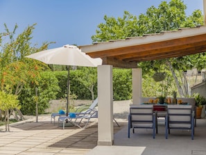 An outdoor patio with a pergola, lounge chairs, and a table set for dining.