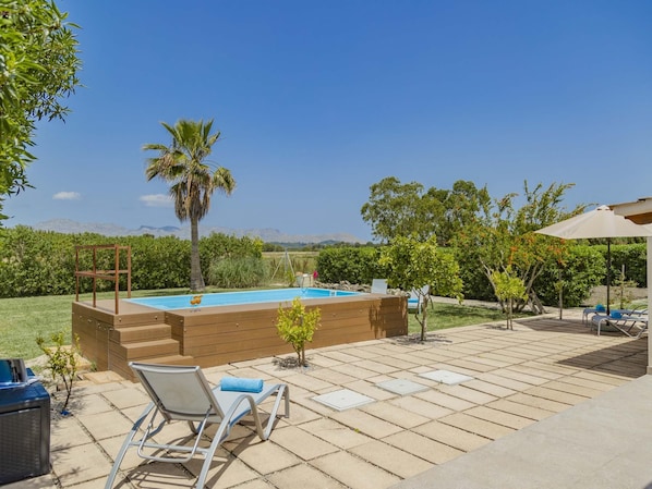 A backyard with a swimming pool, a wooden deck, and a lounge area with chairs.