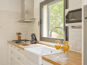 Una cocina moderna con salpicadero de ladrillo blanco, una ventana con vista a follaje, un lavamanos de acero inoxidable y una encimera con cafetera y croissants.