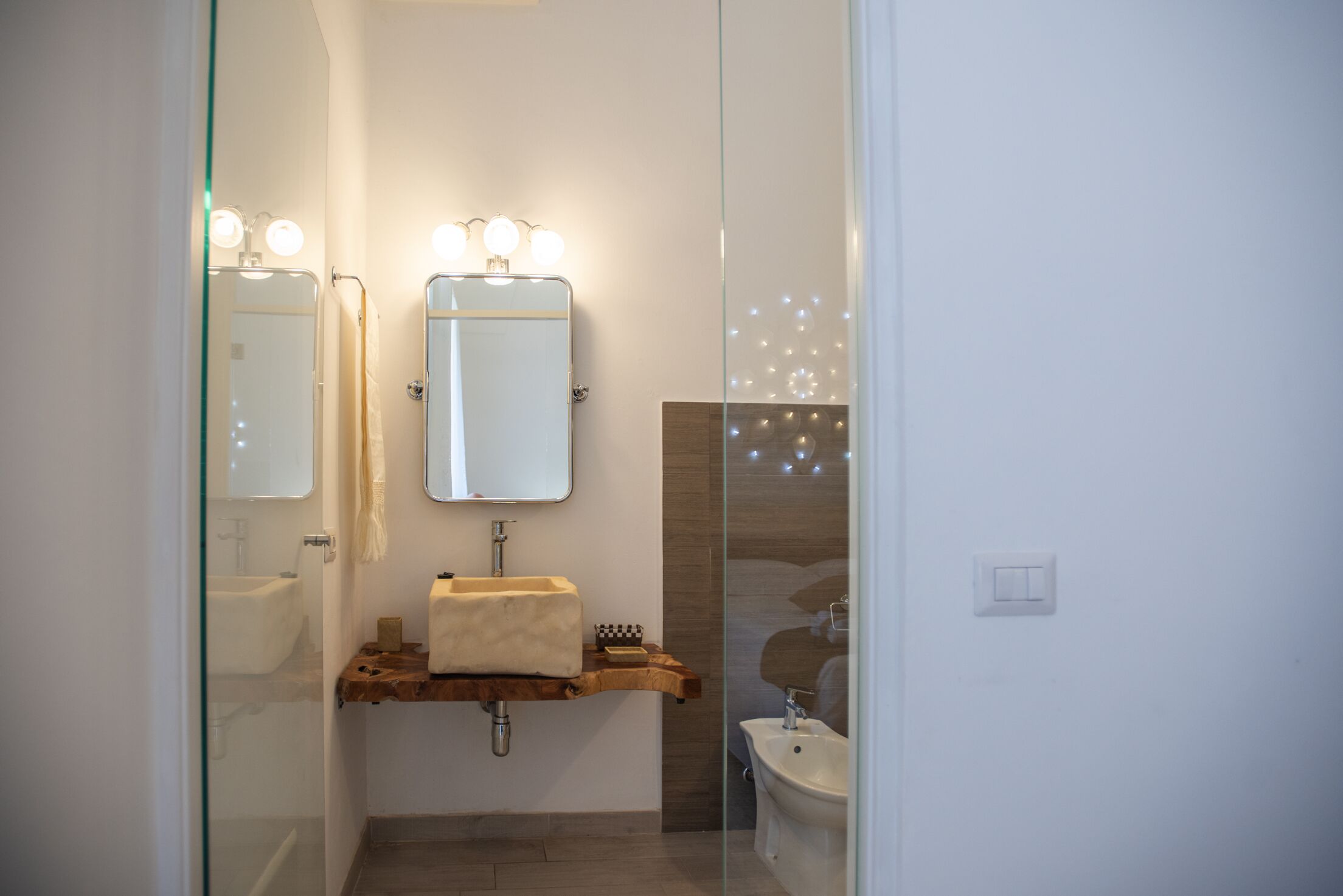 A modern bathroom with a glass shower enclosure, a wooden vanity, and a bidet.