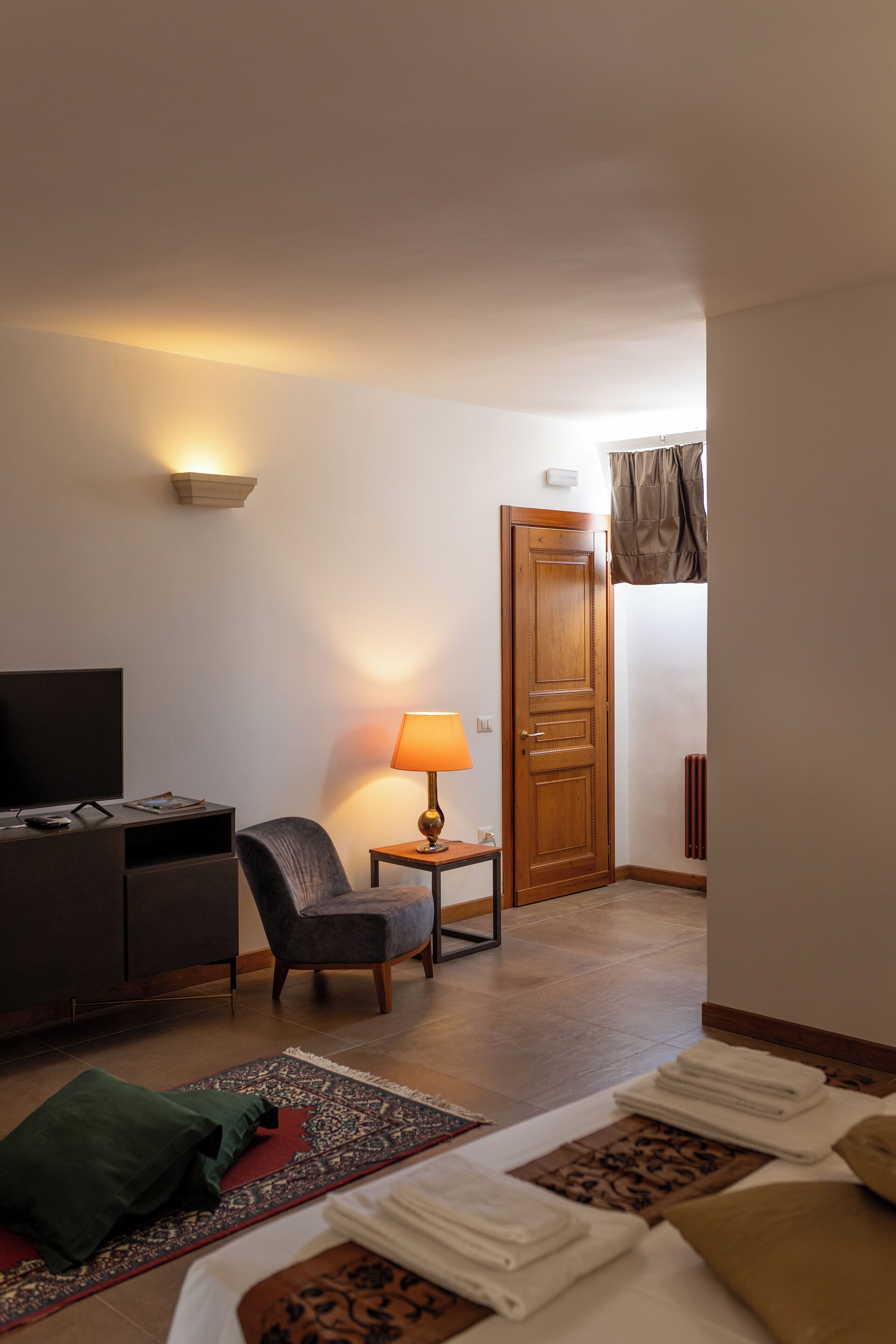 A hotel room with a bed, a TV, a lamp, a chair, and a small table.