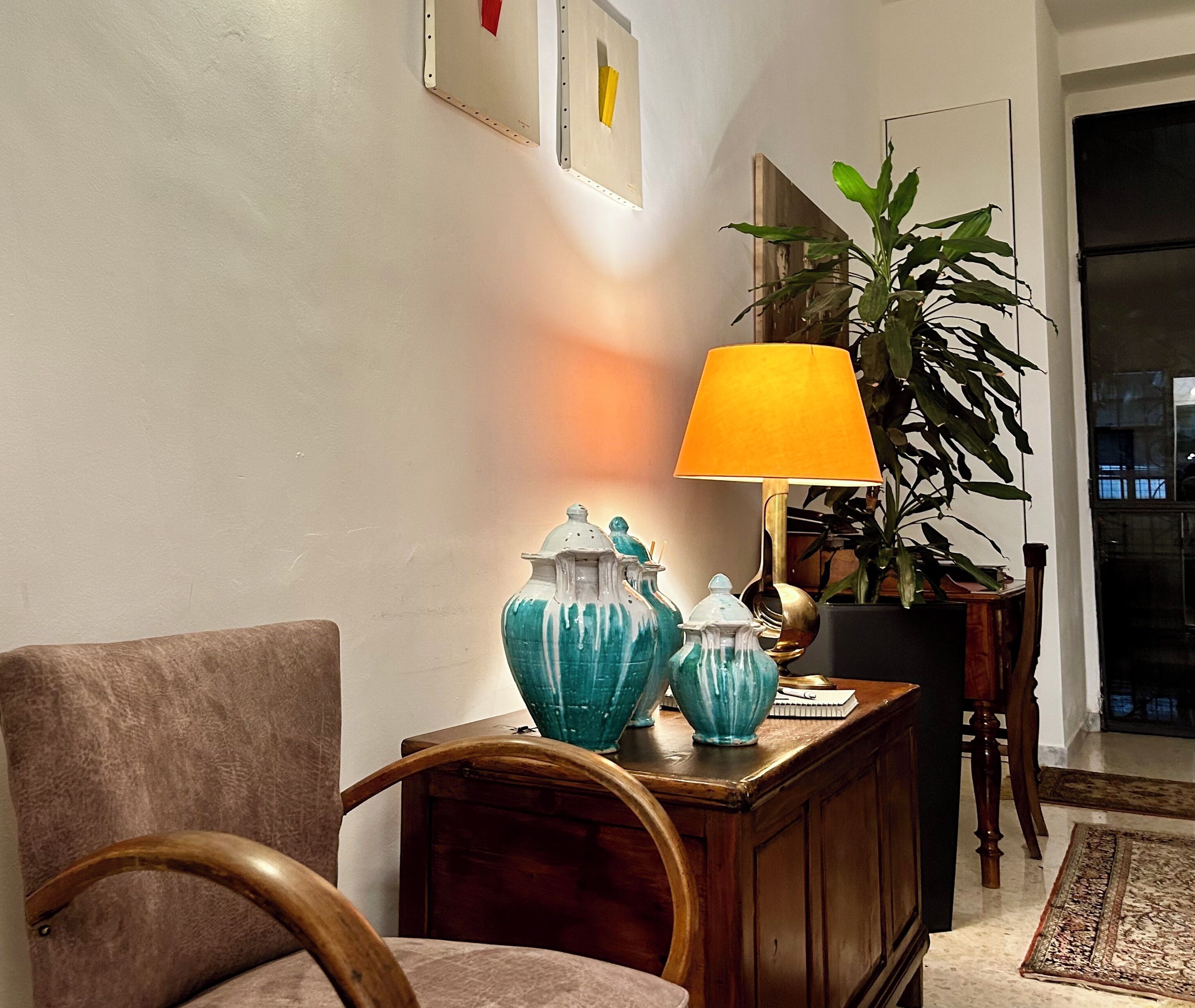Una habitación con una silla de madera, una mesa con jarrones decorativos, una lámpara y una planta en maceta.