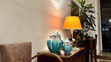 Una habitación con una silla de madera, una mesa con jarrones decorativos, una lámpara y una planta en maceta.