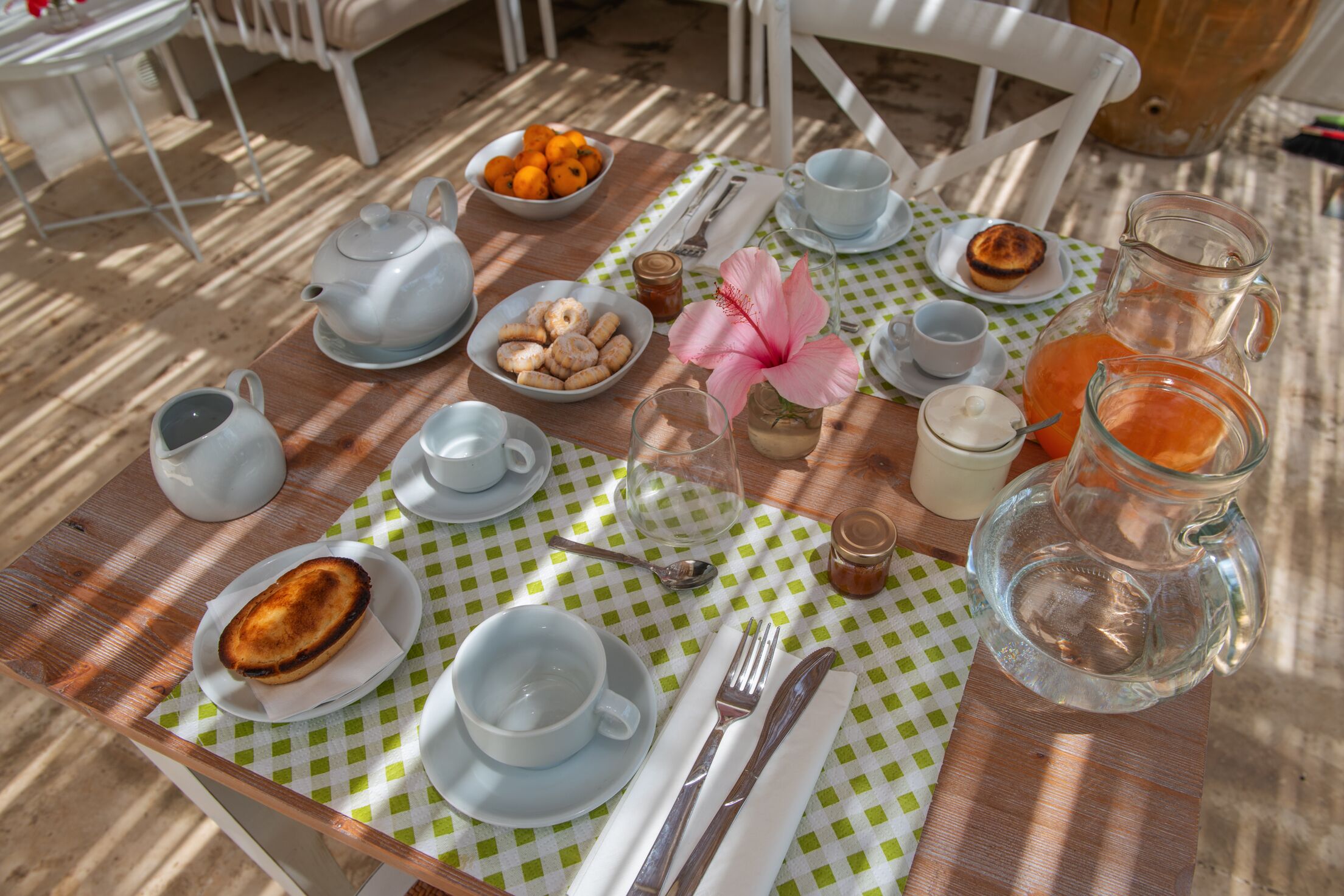 Una mesa dispuesta con alimentos para el desayuno, como una tetera, tazas, una jarra de jugo de naranja y un bol de pasteles.