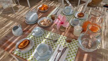 Una mesa dispuesta con alimentos para el desayuno, como una tetera, tazas, una jarra de jugo de naranja y un bol de pasteles.