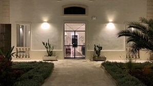 Une entrée bien éclairée, dotée d’une porte grillagée, de plantes en pot et d’un chemin menant à un bâtiment.