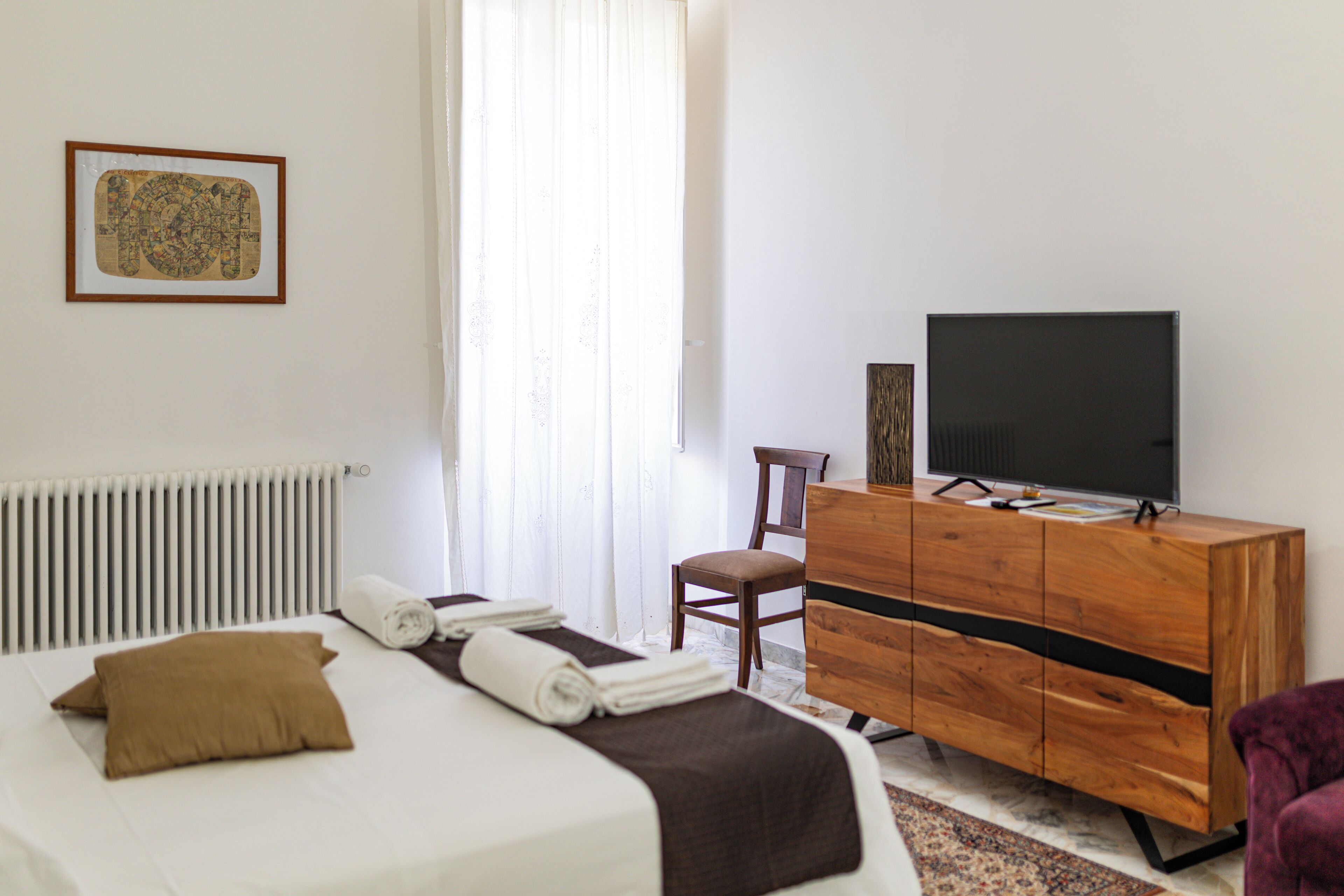 Ein Hotelzimmer mit einem Bett, einem Holzschrank, einem Fernseher und einem Fenster mit Vorhängen.