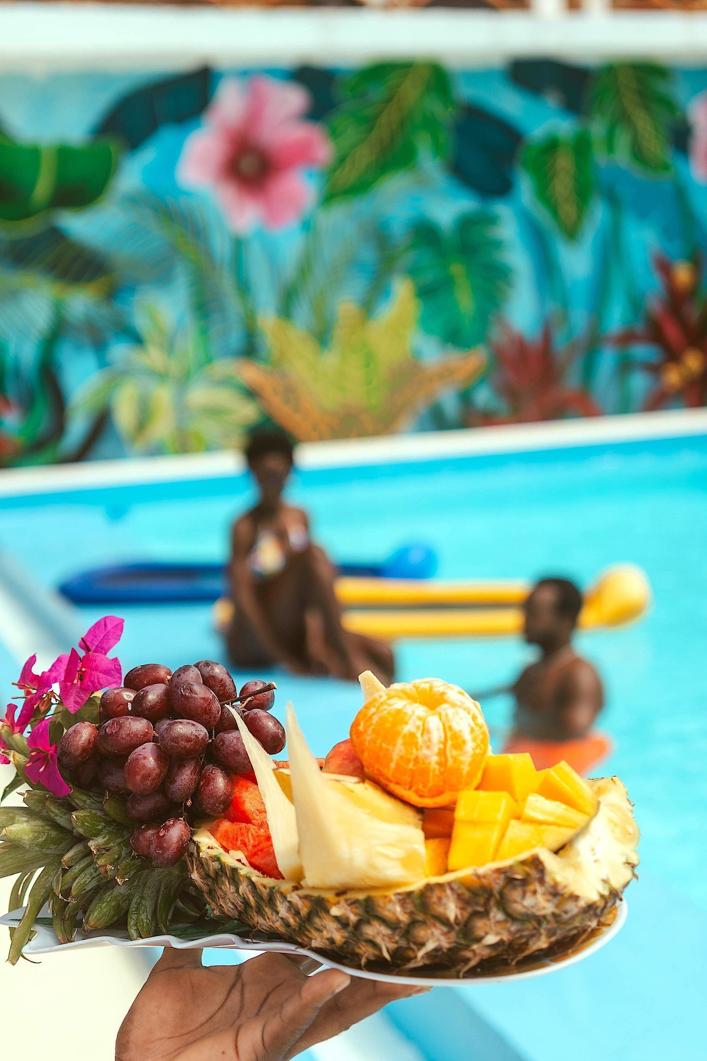 A hand holding a basket with fruits and flowers.