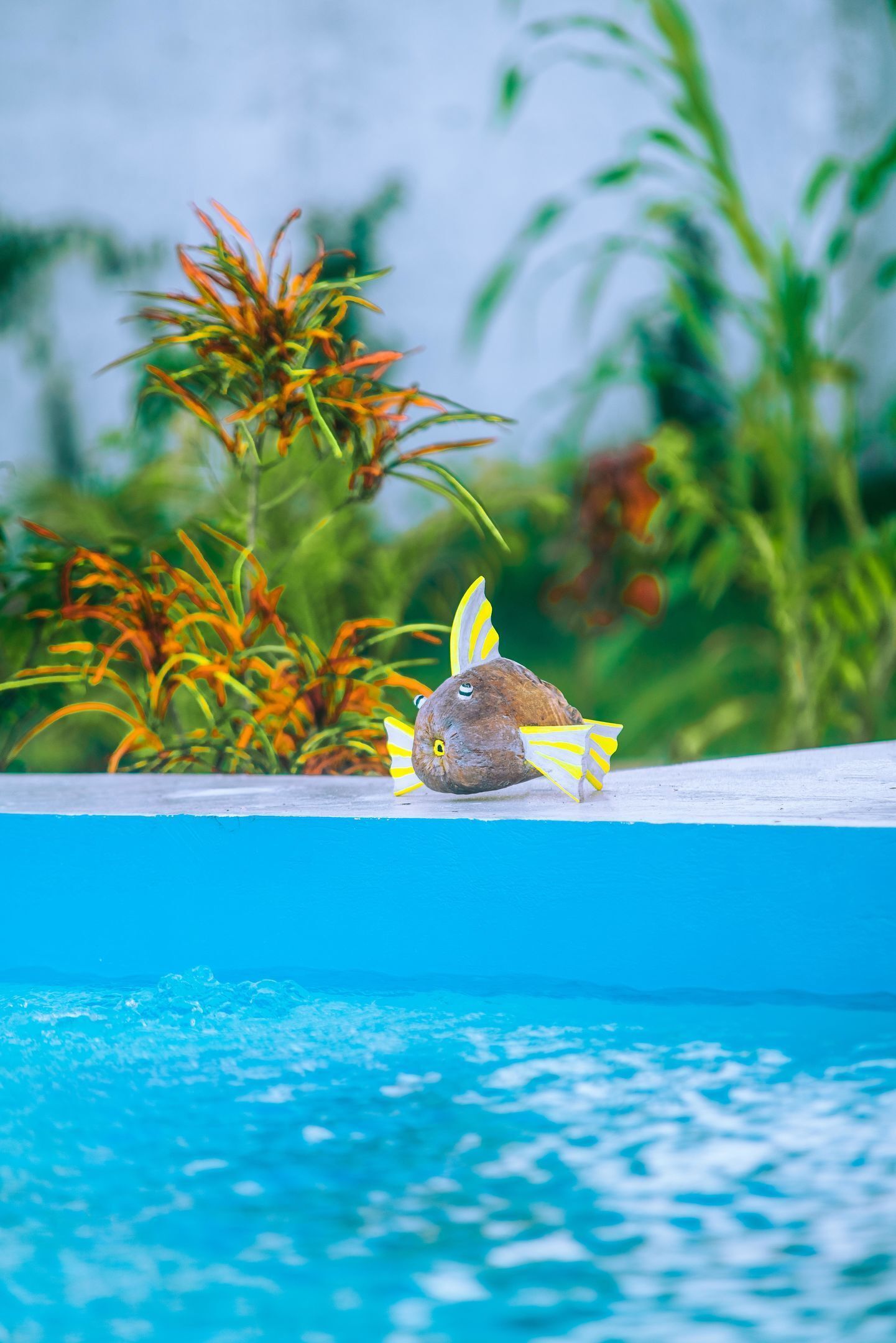A decorative fish sculpture on a pool edge with a blurred background of greenery.