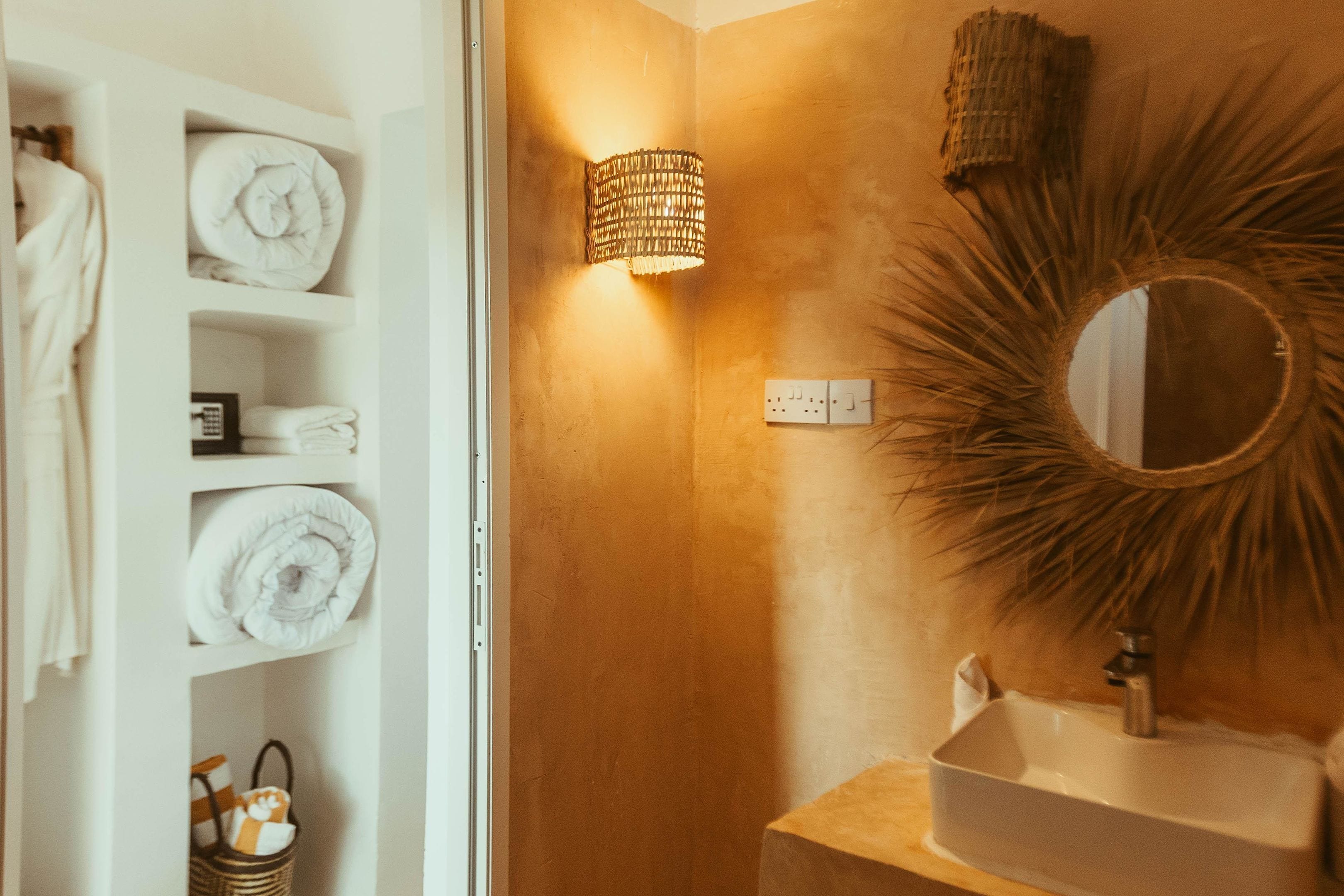 Un baño con un lavamanos blanco, un espejo redondo con un marco de sol y una lámpara de pared.