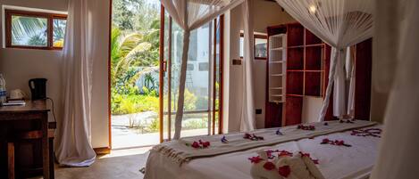 A bedroom with a large bed, a wooden desk, and a view of a garden through the window.