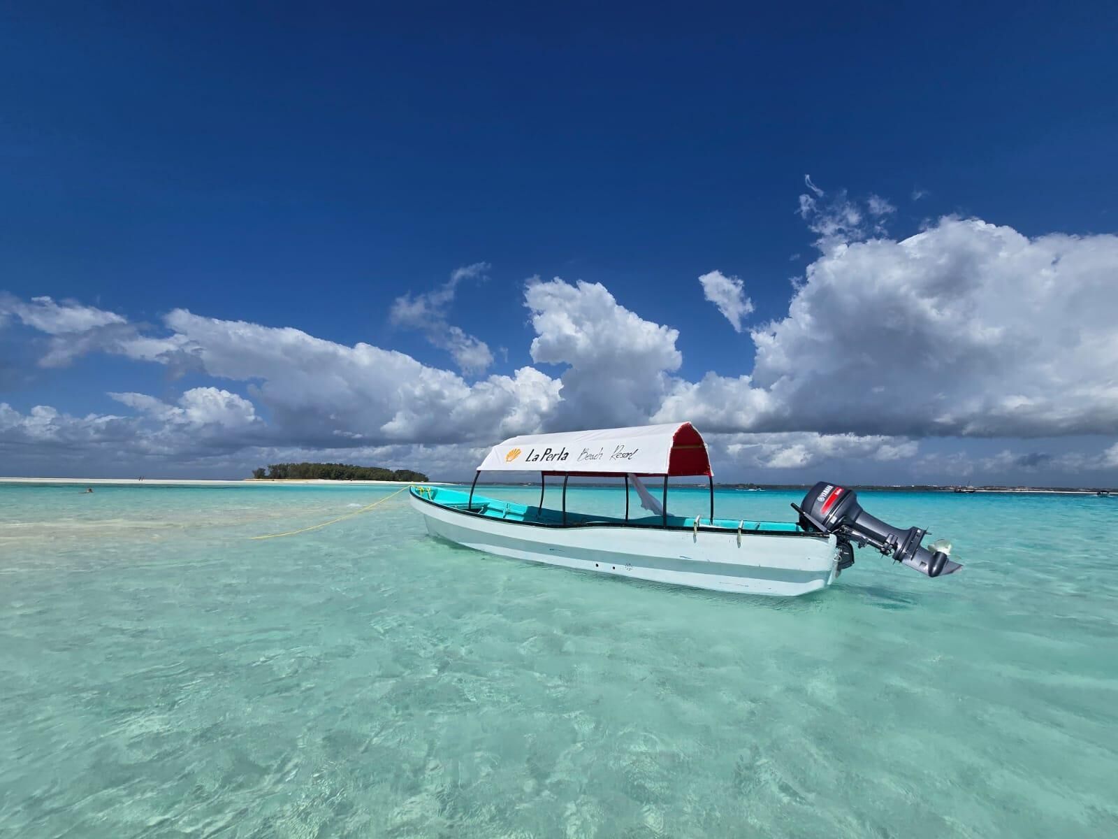 A boat with a canopy labeled "La Perla Beach Resort" anchored in clear turquoise waters.