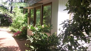 A house with a covered porch, large windows, and lush greenery surrounding it.