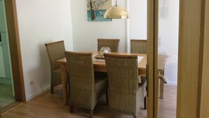 A dining area with a wooden table and wicker chairs, a pendant light, and a painting on the wall.