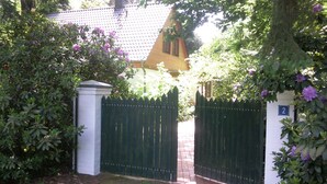 A gated entrance with a brick pathway leading to a house with a tiled roof.